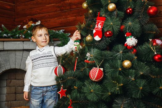 Boy decorates Christmas tree with festive toys and garlands