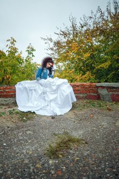 Beautiful bride in wedding dress and denim jacket in autumn park