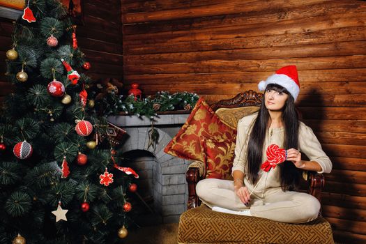 Girl with lollipop in her hand sitting on chair near Christmas tree