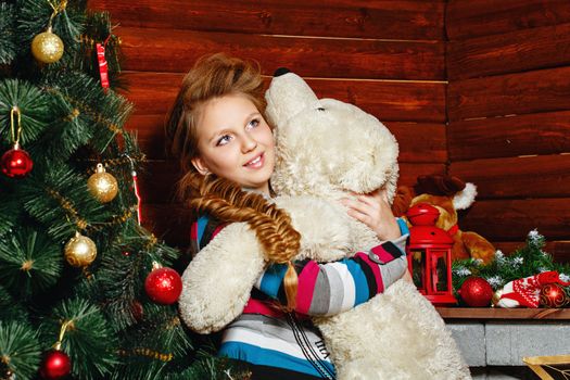 Little girl holding in her hands teddy bear near Christmas tree