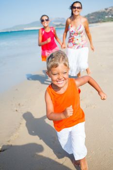 Adorable happy boy with sister and mother running on beach