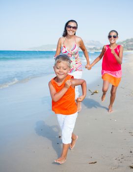 Adorable happy boy with sister and mother running on beach