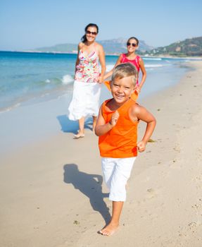 Adorable happy boy with sister and mother running on beach