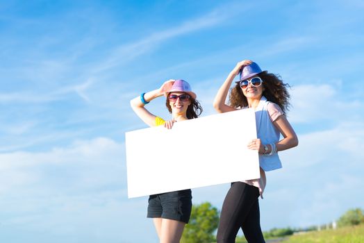 Two young women stand with a blank banner on the side of the road, place for text