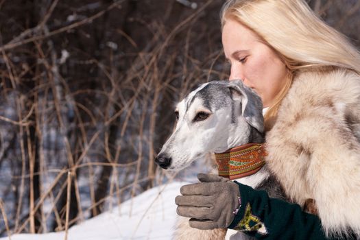 A blonde girl and a grey saluki on snow
