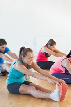 Fitness class and instructor stretching legs in bright exercise room