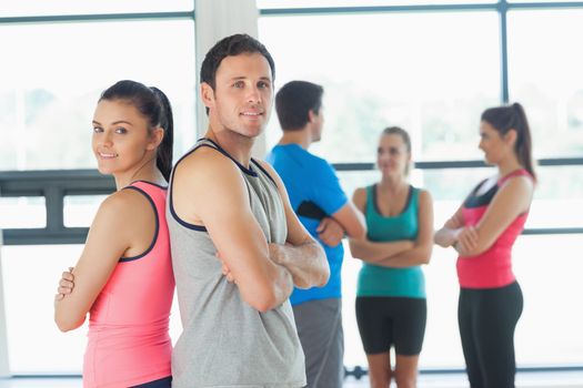 Portrait of a fit couple with friends standing in background in bright exercise room