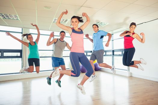 Full length portrait of fitness class and instructor jumping in fitness studio