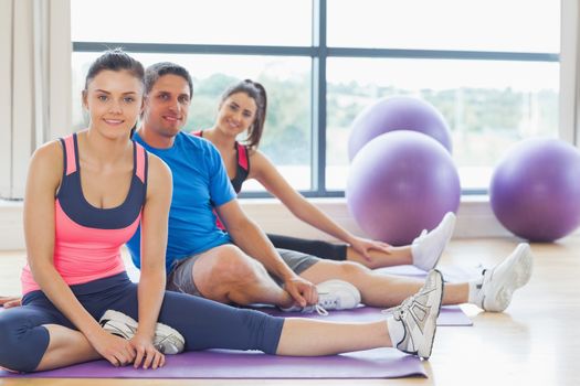 Portrait of smiling class and instructor sitting on exercise mats in fitness studio