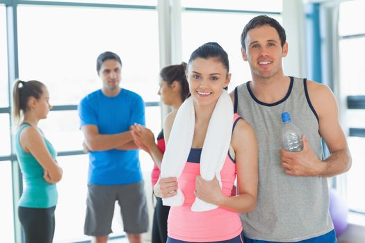 Portrait of a fit couple with friends standing in background in bright exercise room