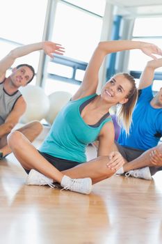 Fitness class and instructor sitting and stretching hands in bright exercise room