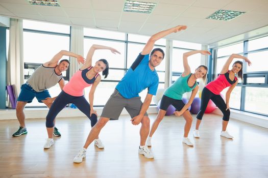 Full length portrait of smiling people doing power fitness exercise at yoga class in fitness studio