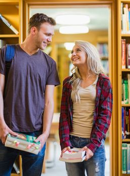 Smiling young couple holding books as they look at each other in the library