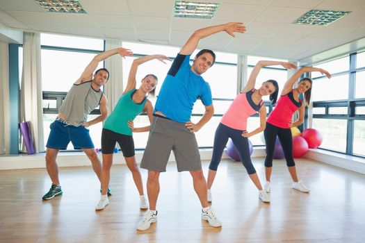 Full length portrait of smiling people doing power fitness exercise at yoga class in fitness studio