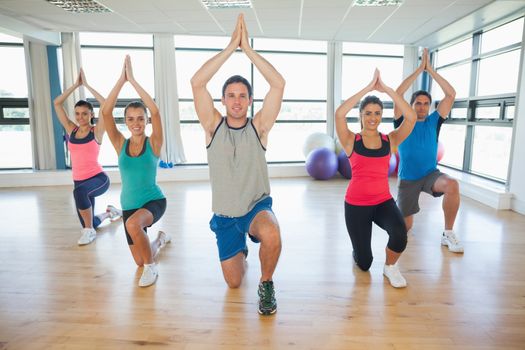 Fitness class and instructor kneeling in Namaste position at exercise studio