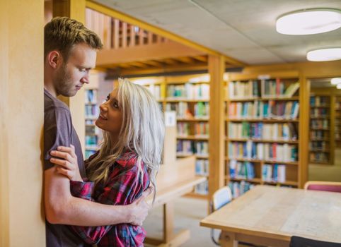 Side view of a young romantic couple looking at each other with bookshelf at a distance in the library