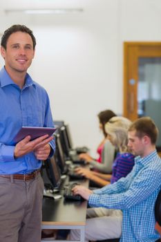 Portrait of a smiling teacher with young college students using computers in the computer room