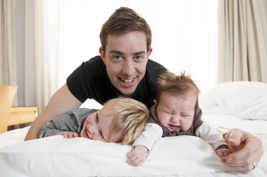 Young father playing with sweet baby girl and little son on bed
