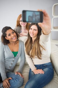 Happy young female friends photographing themselves with smartphone on sofa at home