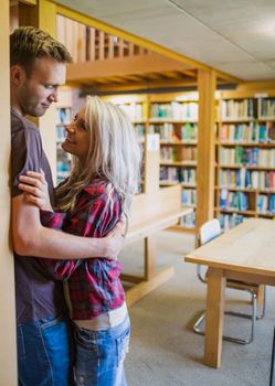 Side view of a young romantic couple looking at each other with bookshelf at a distance in the library