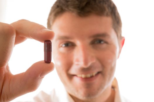 Young Smiling Man holding a Pill in his Hand isolated in White