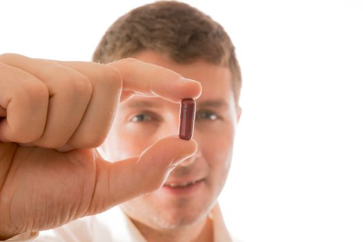 Young Smiling Man holding a Pill in his Hand isolated in White
