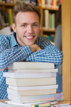 Close up portrait of a smiling male student with stack of books at the college library