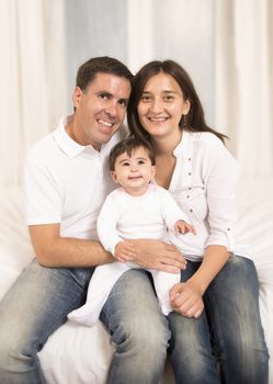 Young couple mother father and baby girl sitting on bed isolated portrait