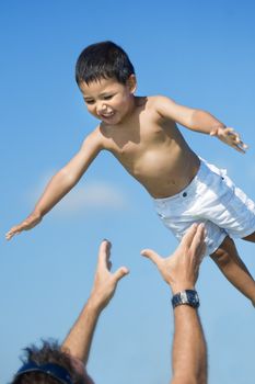 Father playing with his son throwing him to the air in a clear blue sky