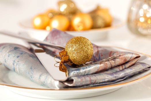 silver cutlery decorated with a golden Christmas bauble, with copy space