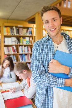 Portrait of a smiling male student with others in background in the college library