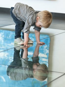 Cute little child playing with his reflexion on the floor
