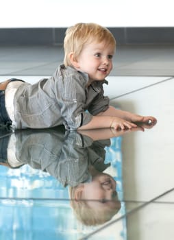 Cute little child playing with his reflexion on the floor