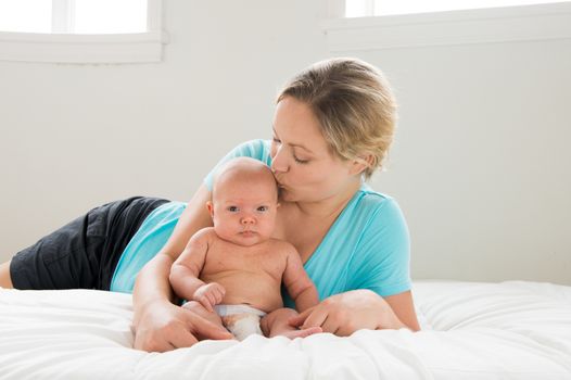 A happy Mother wearing blue shirt kissing her baby boy on  a  white background