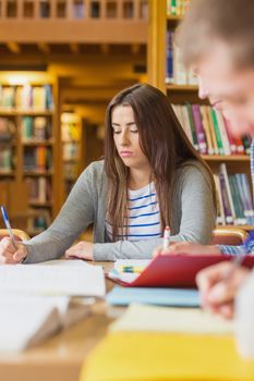 Young female student writing notes at desk in the college library