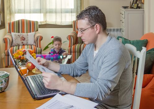 Father reading business documents in home office and his boring son playing on the background
