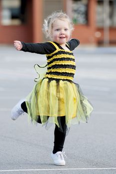 Happy blond little girl in bee costume dancing and playing outdoors