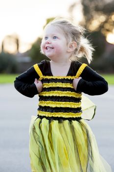 Happy blond little girl in bee costume dancing and playing outdoors