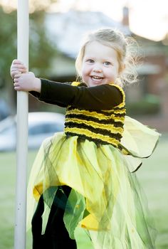 Happy blond little girl in bee costume dancing and playing outdoors