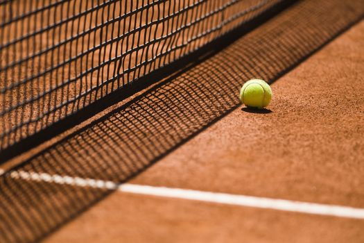 Tennis ball next to the net shot with a shallow depth of field on a clay court