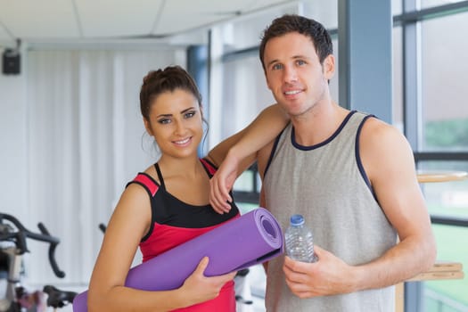 Portrait of a fit young couple with water bottle and exercise mat in a bright exercise room
