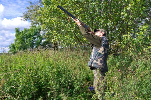 Man hunter aiming flying pigeons with shotgun