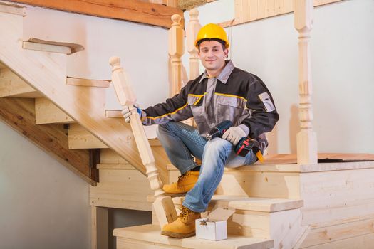 worker sitting on ladder holding wooden post and cordless drill
