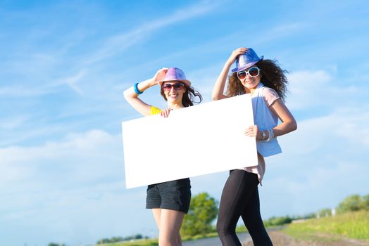 Two young women stand with a blank banner on the side of the road, place for text