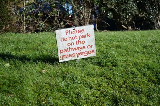 No parking sign on a verge beside a pathway asking for road users not to park on the grass.