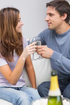 Romantic smiling young couple toasting flutes in the living room at home