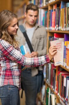 Pretty student taking book from shelf in library at the university