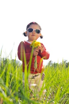 Little girl in sunglasses with dandelion flowers outdoors