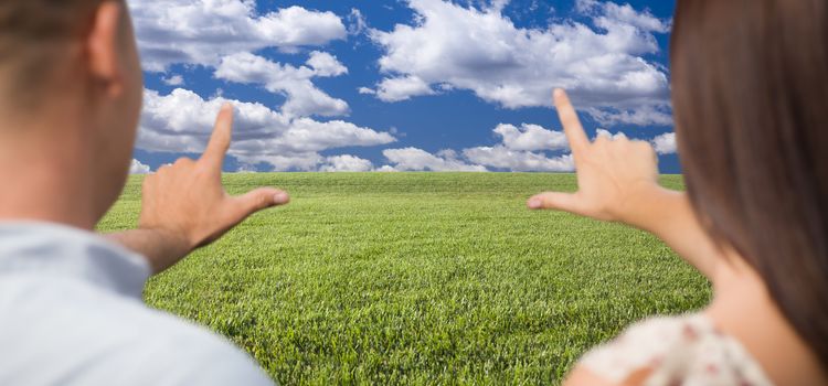 Couple Framing Hands Around Space in Grass Field and Sky on the Horizon.