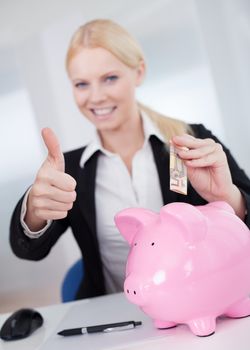 Businesswoman holding euro currency and piggybank in the office